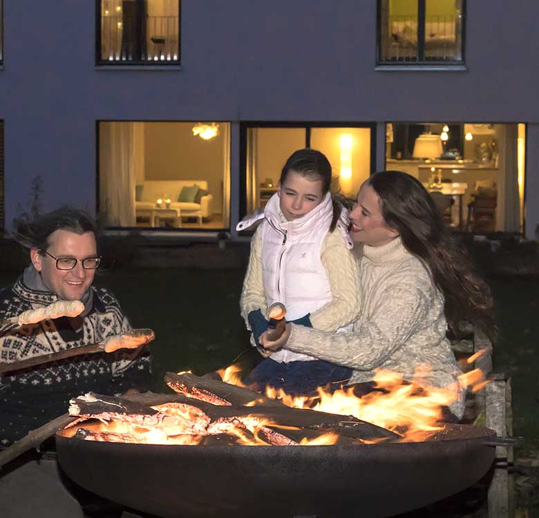 Eine Familie im Dunkeln, backt Stockbrot am Lagerfeuer vor dem Haus