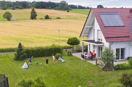 Symbolbild für Bauen, Kaufen, Mieten: ein neu gebautes Haus im Grünen, davor spielende Kinder