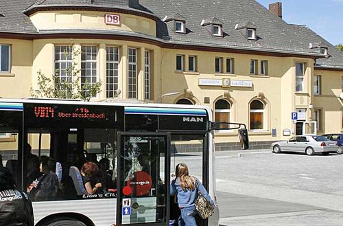 Symbolbild für Mittendrin: Der Bahnhofsvorplatz in Alsfeld, im Vordergrund steigen Kinder in e inen Bus