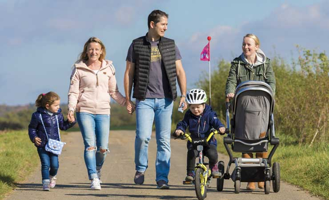Familie mit Kleinkind auf dem Rad und einem Kinderwagen ist draußen bei Sonnenschein unterwegs