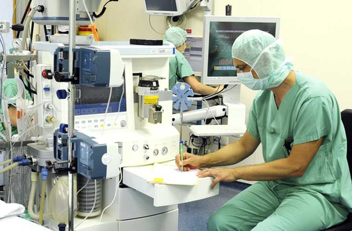 Symbolbild für ärztliche Versorgung: Krankenhaus- oder Labormitarbeiter in grüner Kleidung mit Masken und Schutzhauben