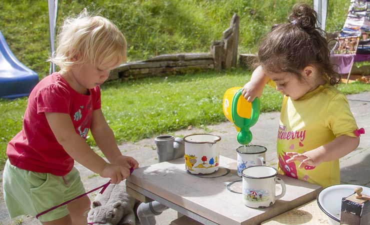 Zwei etwa dreijährige Mädchen spielen an einem Kindertisch im Garten