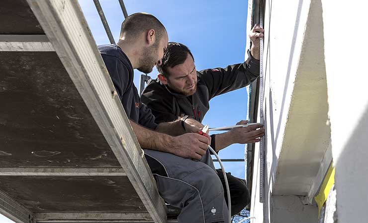Zwei Männer auf einem Fassadengerüst beim Verlegen von Leitungen