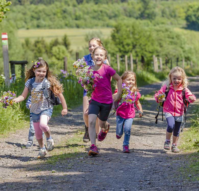 Fünf Mädchen haben im Feld Blumen gepflückt und laufen einen Feldweg entlang