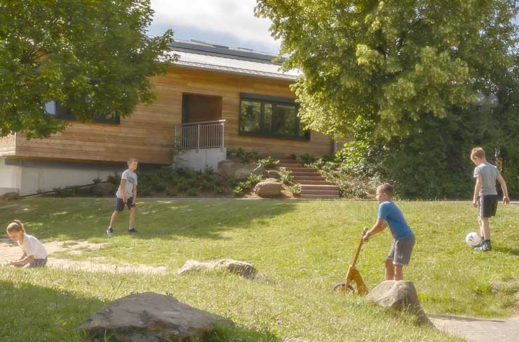 Symbolbild für Kinderbetreuung: Ein modernes Schulgelände, Kinder schaukeln, fahren Roller und spielen Fußball