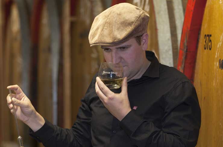 Symbolbild für Arbeiten: Destillateur mit Baskenmütze riecht an einer Probe im Glas