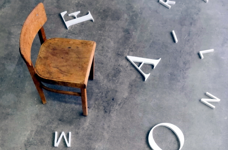 Symbolbild Kultur: Ein leerer Stuhl im Raum, Buchstaben auf dem Boden
